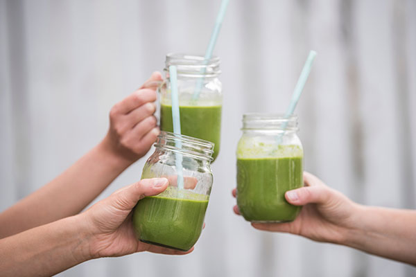 Three people clicking glasses of green smoothies